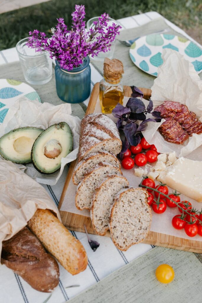 A vibrant picnic spread featuring fresh baked bread, cherry tomatoes, avocados, and salami on a wooden table outdoors in Italy.