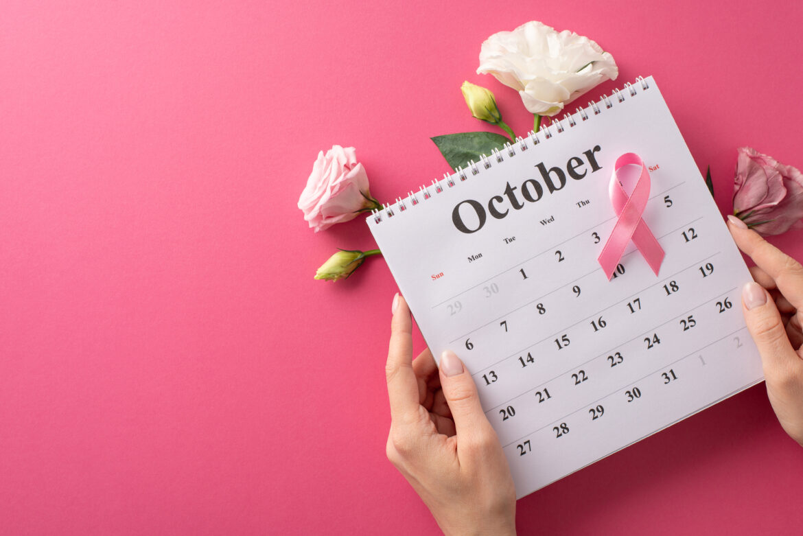 Emphasizing Breast Cancer Awareness Month. Top-down view of female hands embracing a calendar Roze oktobar