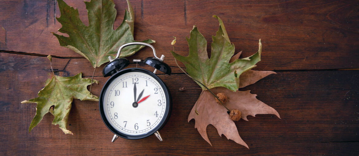 Fall Back, Daylight Saving Time. Yellow clock and autumn leaves on wood Letnje računanje vremena