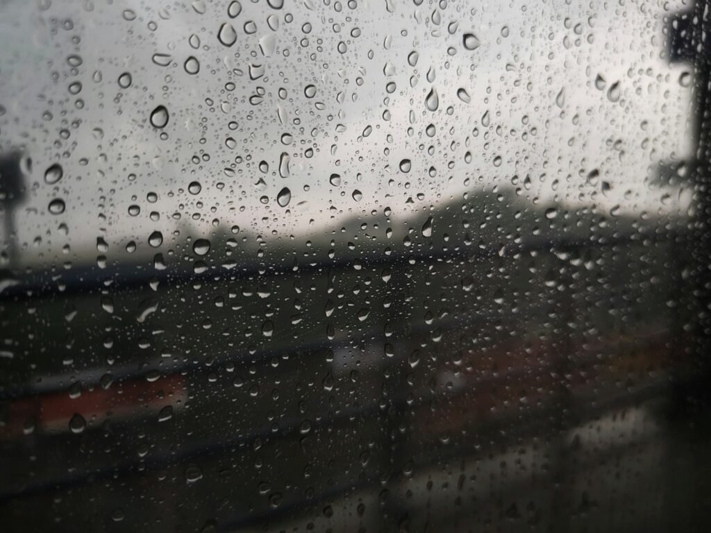 Kapljice kiše na prozoru sa zamućenom pozadinom,