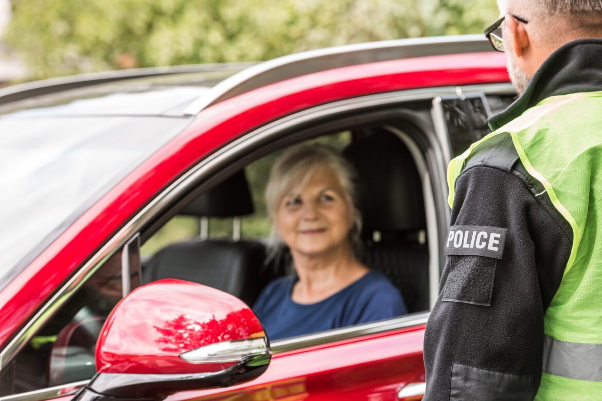 Policeman talks to an elderly lady sitting in a luxurious red car obustava saobraćaja